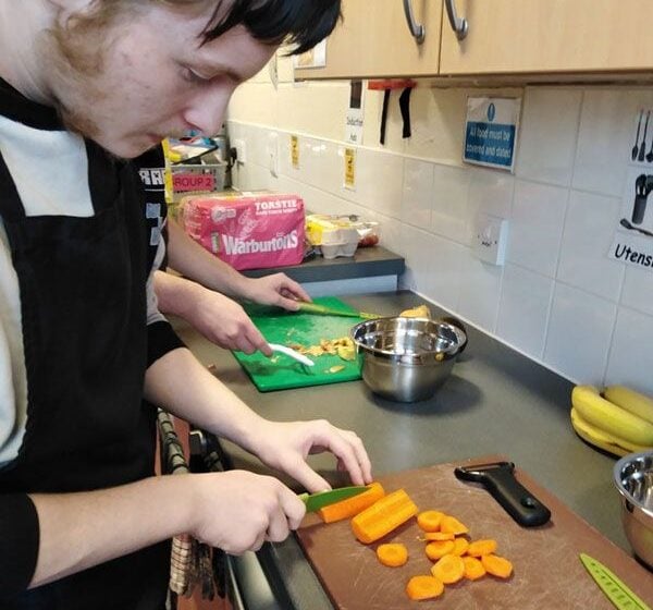 Young man chopping up carrots on a kitchen work top.