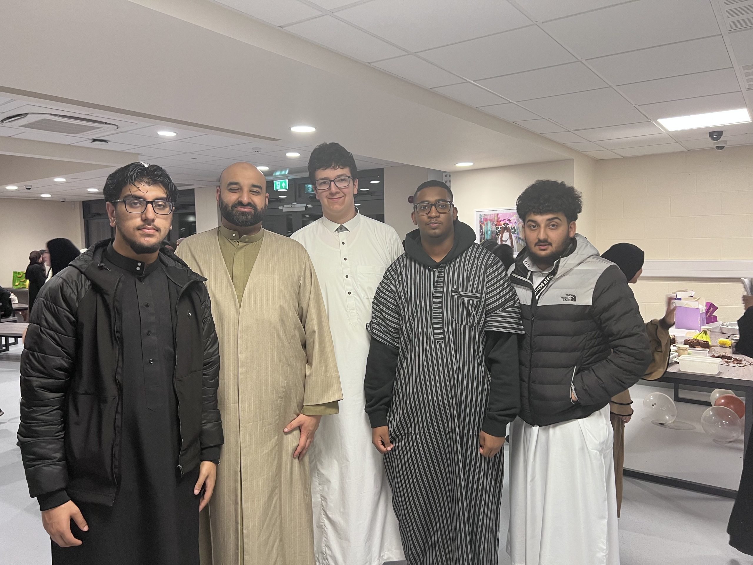 5 Muslim males of various ages posing for the camera inside the college cafeteria