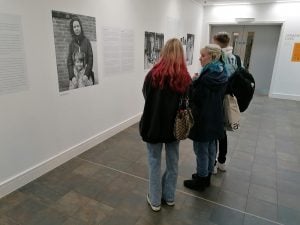 Three students looking at large photos and text hung on the gallery wall.