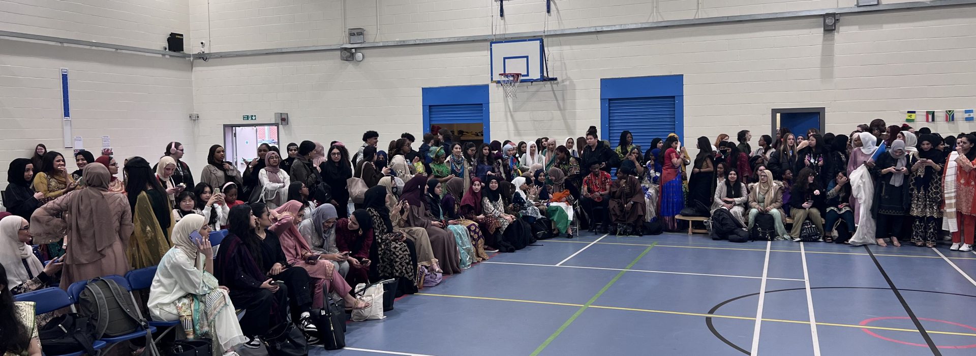 young student dressed in a variety of culture attire sitting patiently in the sports hall waiting for the show to start