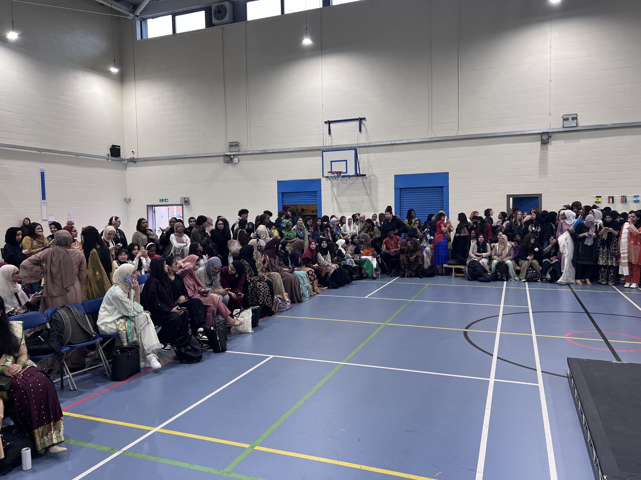 young student dressed in a variety of culture attire sitting patiently in the sports hall waiting for the show to start