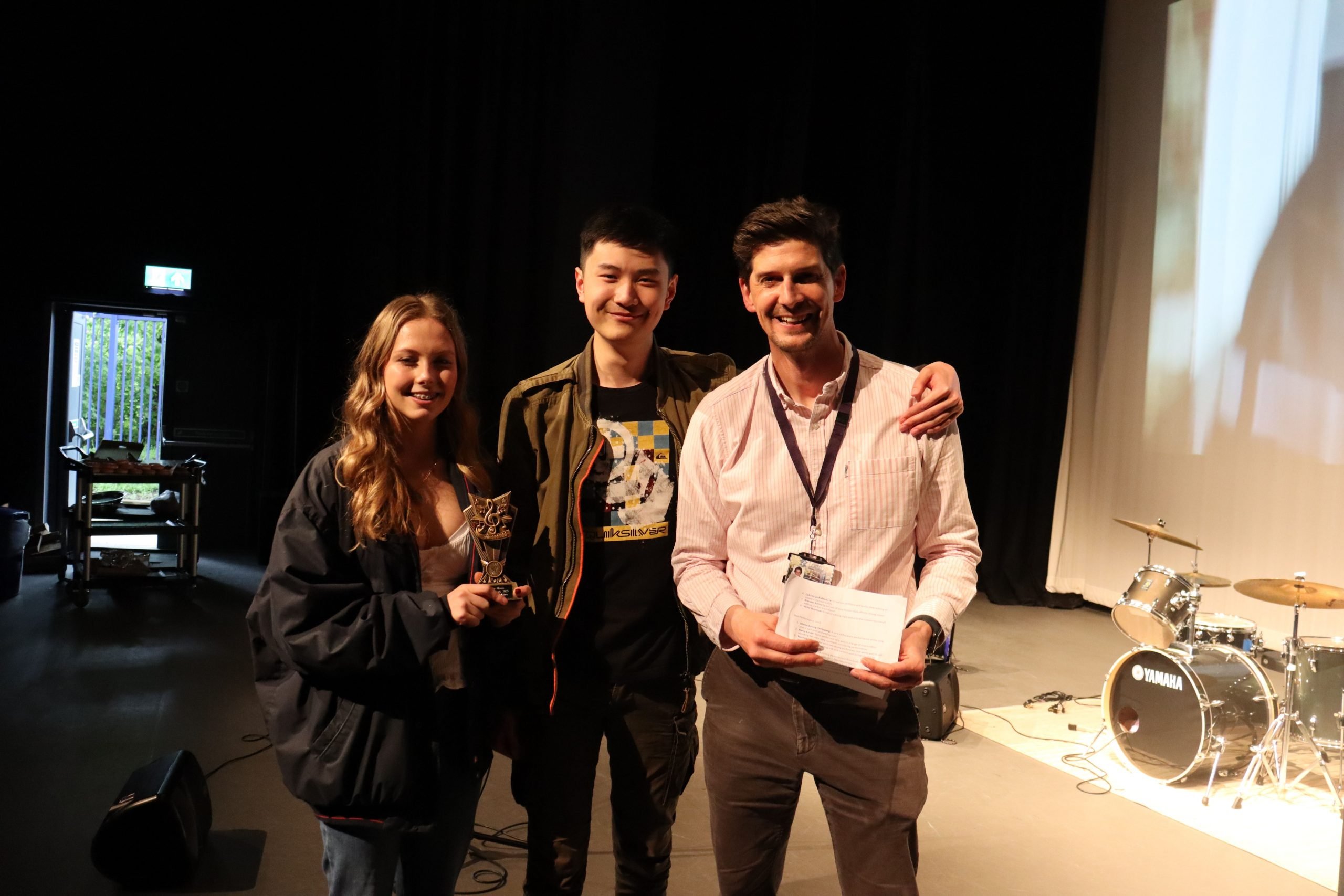 Two smiling students holding their award, stood alongside their teacher.