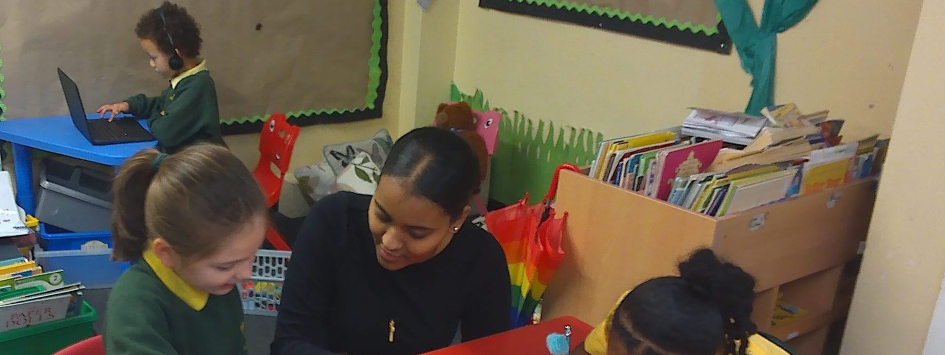 Student in a classroom, helping a couple of children with their work.