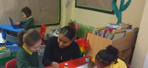 Student in a classroom, helping a couple of children with their work.