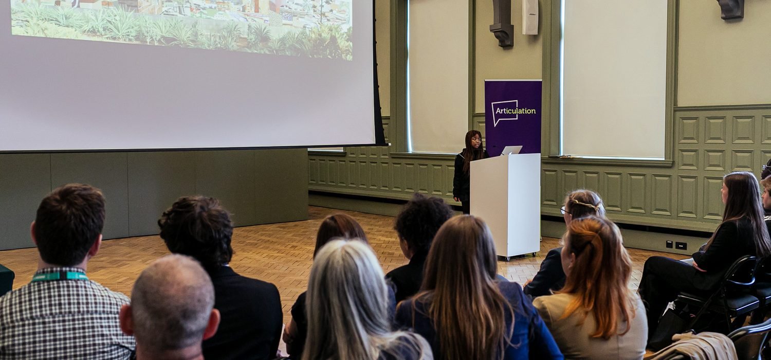 Young student delivering a presentation at a lectern in front of an audience inside an art gallery.