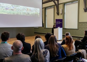 Young student delivering a presentation at a lectern in front of an audience inside an art gallery.