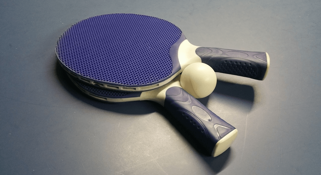 Picture of 2 blue table tennis bats laying on top of each other, with a and table tennis ball inbetween.