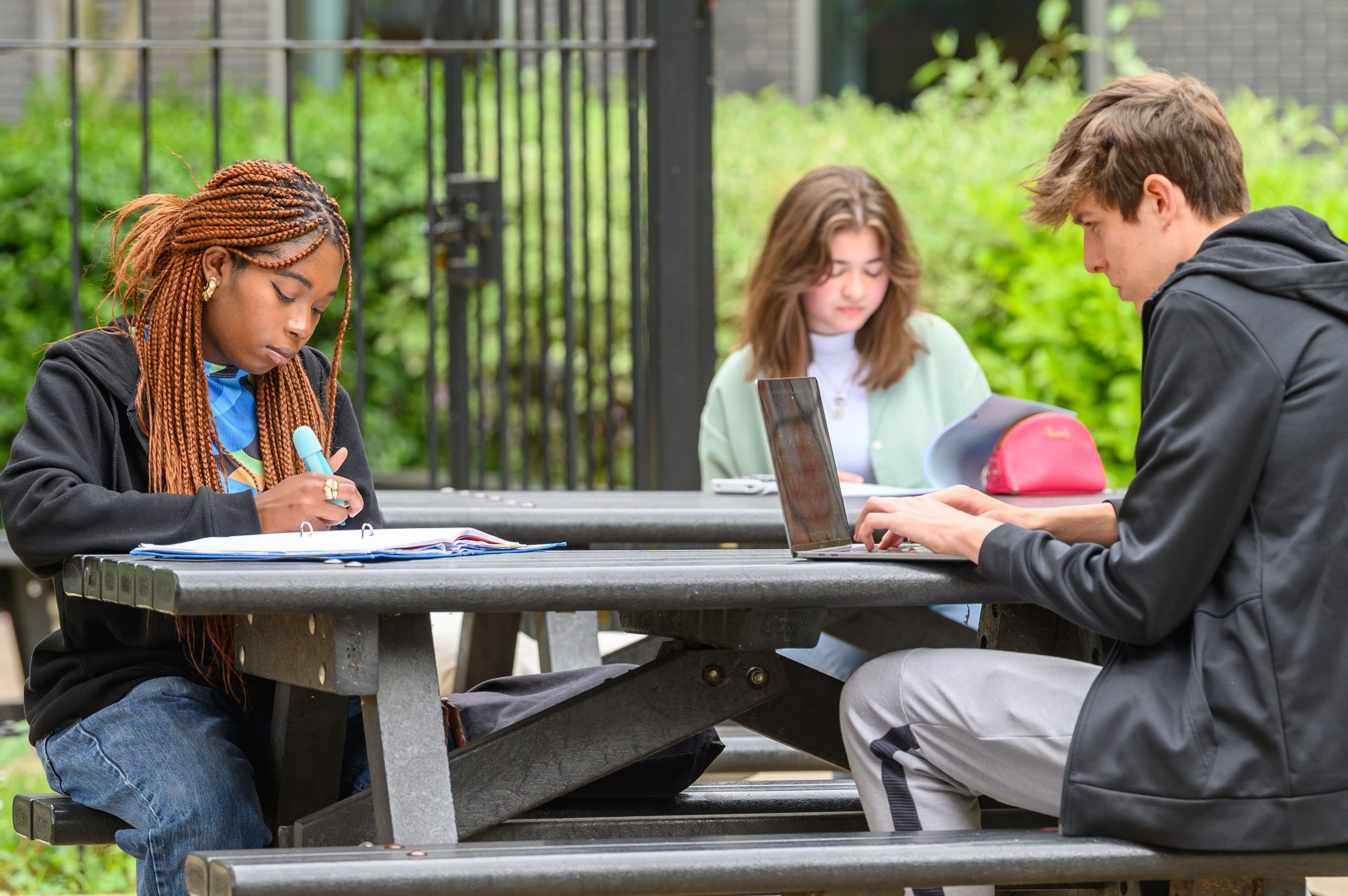 Three students working outside sat on a bench.