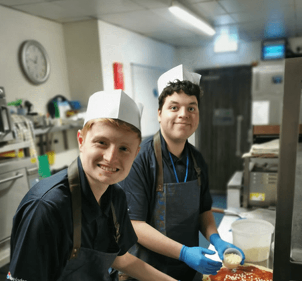Two young male students preparing pizzas in the kitchen of The Travelodge Hotel.