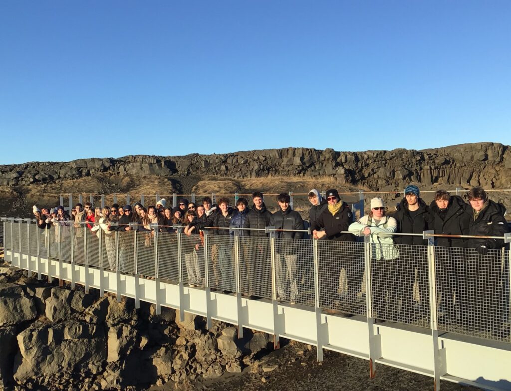 Loreto College group standing on a footbridge in a rocky Icelandic landscape under a clear blue sky.