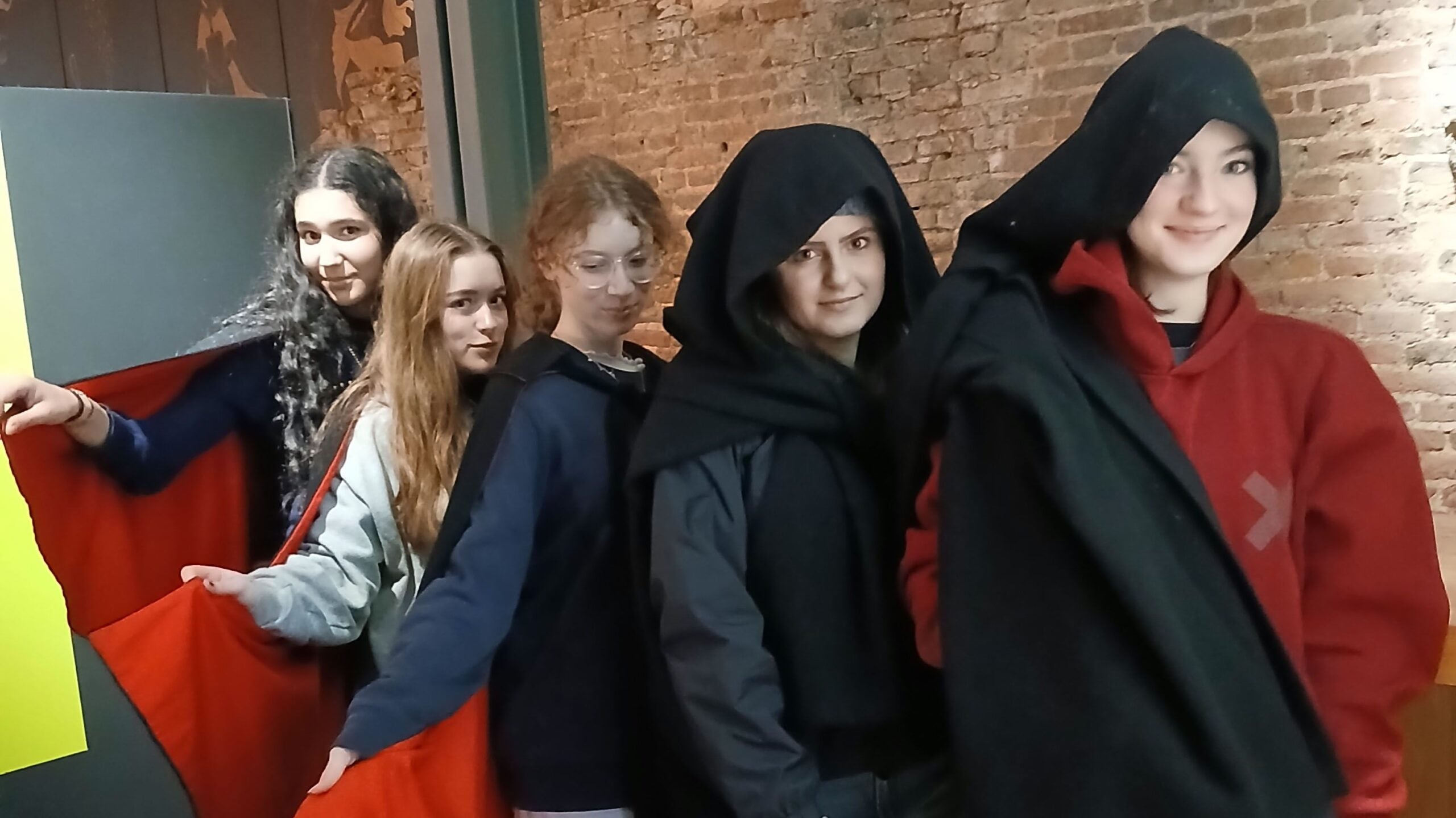 Group of Loreto College students standing indoors wearing dark cloaks as part of an interactive English department activity during a Whitby visit.