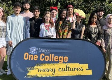 Students in traditional dress at Loreto College Manchester celebrating cultural diversity during Cultural Appreciation Day, with “One College many cultures” sign.