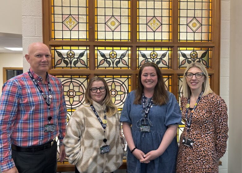 Four members of the Loreto College careers team standing in front of a decorative stained glass window inside the college building.