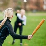 Woman playing rounders, holding a bat and preparing to hit the ball during an outdoor game on a grass field.