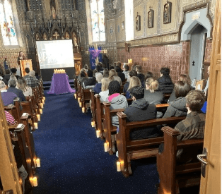 The interior of a 19th Century chapel with a congregation of people sat during a Catholic Mass