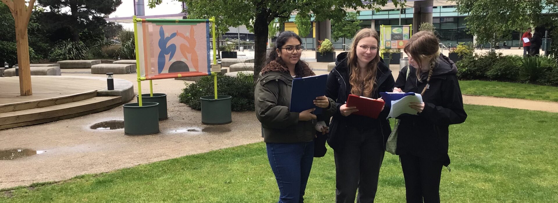 Three students carrying clipboards and worksheets during an outdoor fieldwork activity a Salford Quays.
