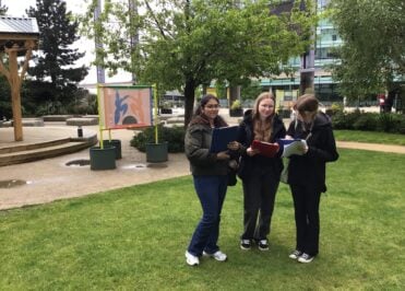 Three students carrying clipboards and worksheets during an outdoor fieldwork activity a Salford Quays.