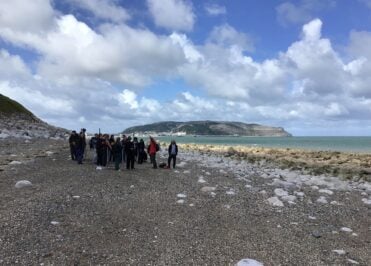 A group of Loreto Geography students standing on a rocky beach in Llandudno with the Great Orme headland visible across the bay.