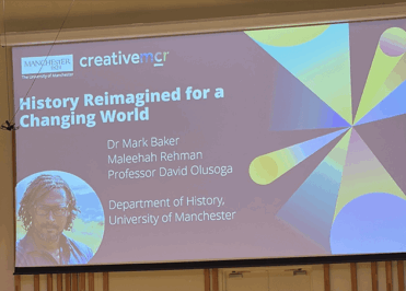 Presentation slide titled “History Reimagined for a Changing World” from the University of Manchester Department of History, displaying speaker names and a portrait image on a lecture theatre screen.