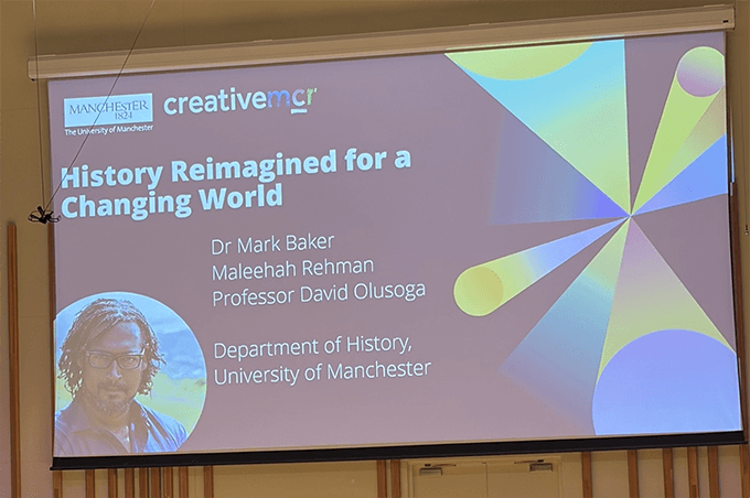Presentation slide titled “History Reimagined for a Changing World” from the University of Manchester Department of History, displaying speaker names and a portrait image on a lecture theatre screen.