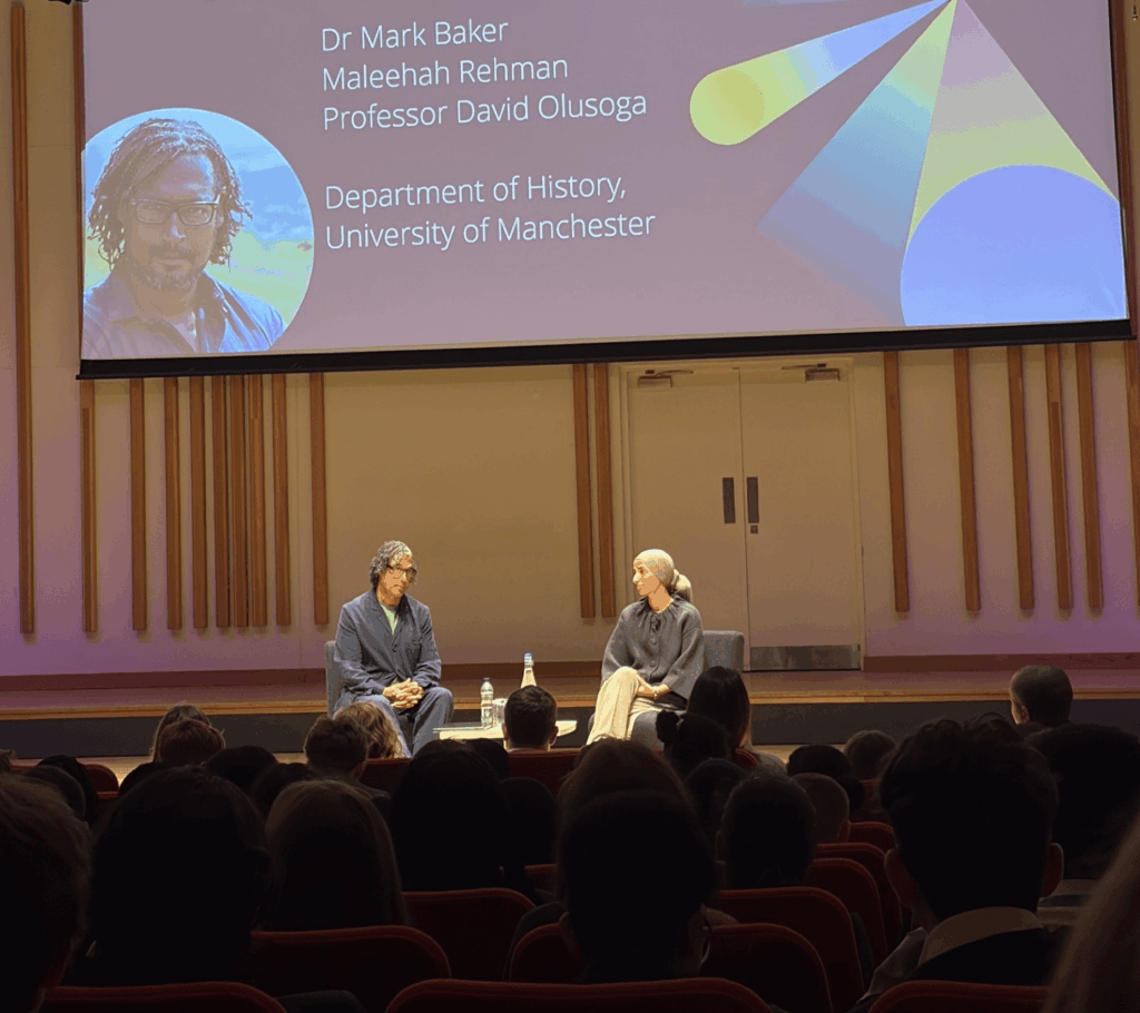 Audience members listen to a live discussion during the Loreto College History Trip, with a large presentation screen displaying “History Reimagined for a Changing World” at the University of Manchester.