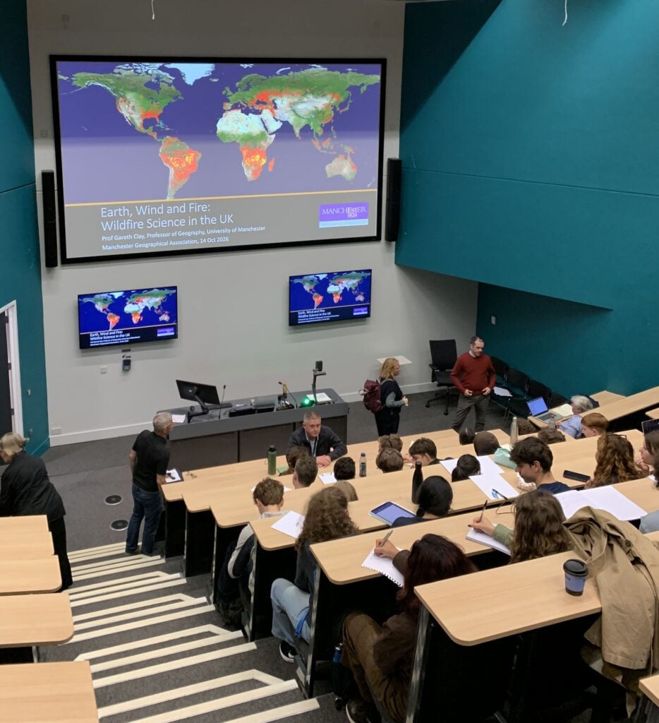 Students attending a wildfire science lecture in a university lecture theatre, with a presentation on global wildfire patterns displayed on a large screen.